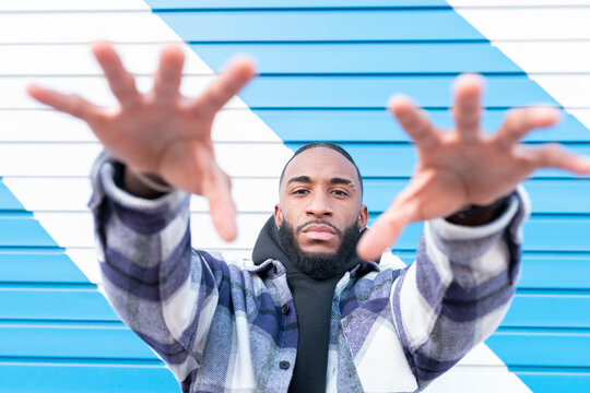 Young man with cool attitude gesturing against blue and white corrugated wall