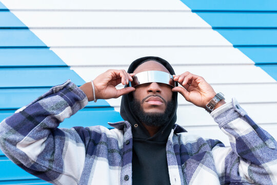 Young male rapper with arms raised wearing sunglasses against corrugated iron