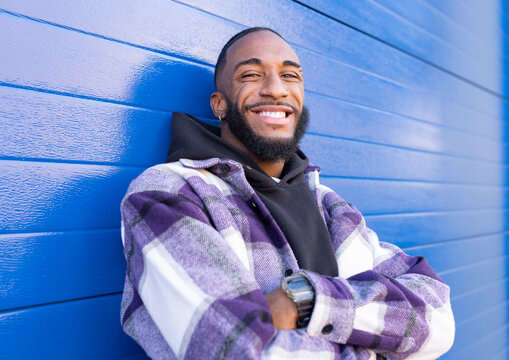 Young male rapper with arms crossed standing against blue corrugated wall