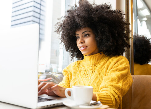 Curly hair woman using laptop while sitting at cafe