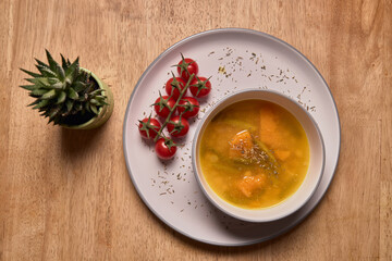 Vegetable soup or broth with pumpkin and chickpeas in a bowl. fine spreading herbs. solid wood background. Healthy, vegan and diet food. tasty recipe