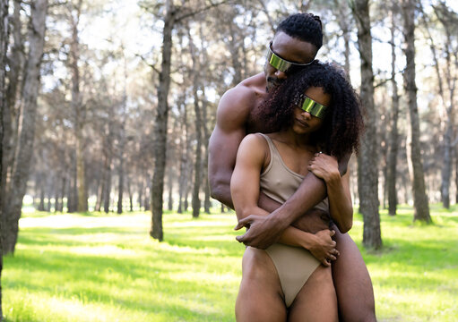 Two professional dancers wearing futuristic goggles embracing in middle of forest
