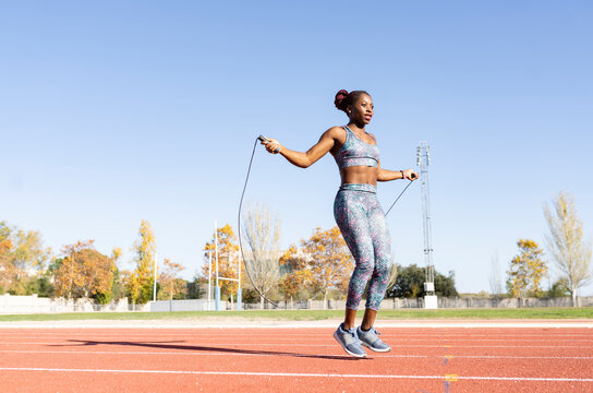 Female sportsperson skipping with jump rope over running track on sunny day