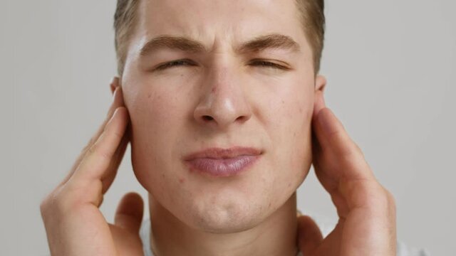 Middle ear inflammation. Close up of young man suffering from ear pain, shouting from ache, slow motion