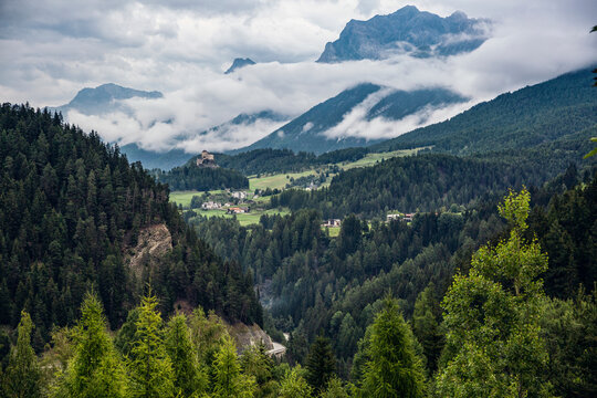 Switzerland, Canton Of Grisons, Scuol, Green forested valley with Tarasp Castle in distant background