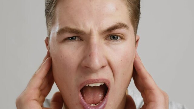 Increased hearing sensitivity. Close up of young man suffering from noise, rubbing ears, slow motion