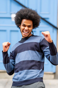 Excited young man with curly hair gesturing while standing against wall