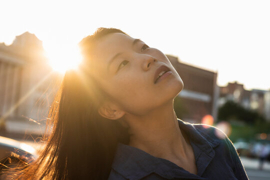 Close-up of beautiful woman looking up against bright sunset sky during weekend