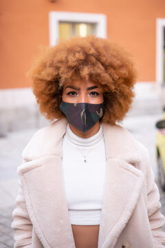 Mid adult woman with afro hair wearing face mask while standing against building