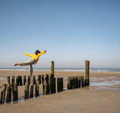 Mature woman with arms outstretched balancing on wooden posts at beach against clear sky