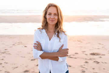Smiling woman standing with arms crossed at beach