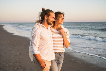 Smiling young couple looking away while walking at beach during vacation