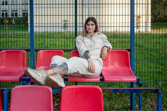 Young woman posing while sitting on seat against fence in sports court