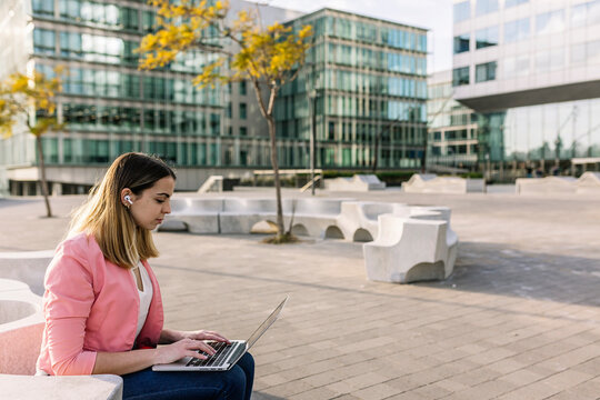 Spain, Barcelona, Young businesswoman using laptop in front of office buildings