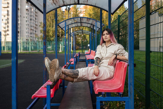 Fashionable young woman with cool attitude sitting on red seat in sports court