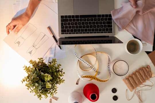 Fashion designer examining fabric swatch and design by laptop at desk in atelier