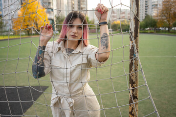 Hipster woman with tattoo seen through goalpost net in soccer field