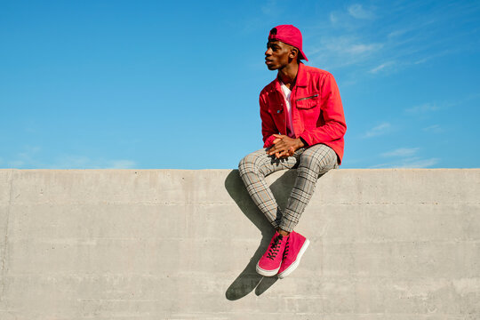 Young man in red jacket and baseball cap sitting on concrete wall