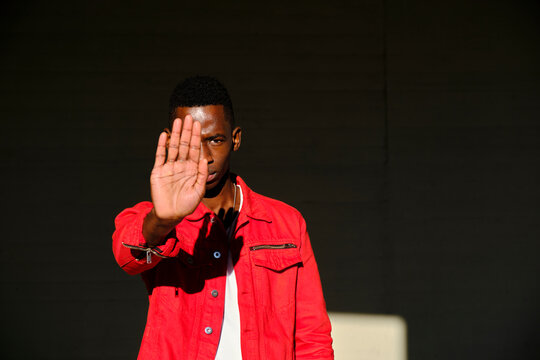 Young man in red jacket making stop gesture in sunlight