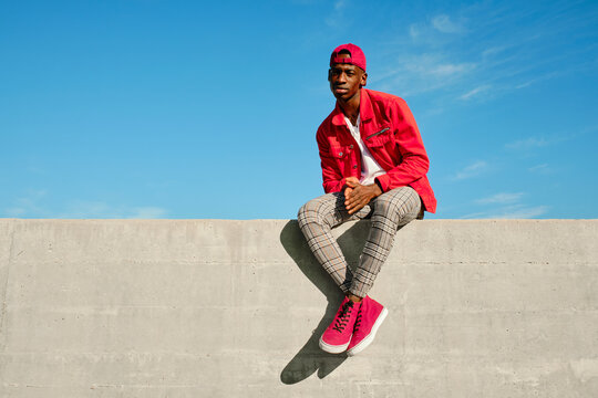 Young man in red jacket and baseball cap sitting on concrete wall