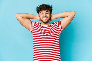 Young arab man on blue background feeling confident, with hands behind the head.