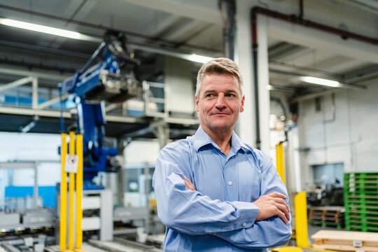 Smiling supervisor with arms crossed looking away in industry