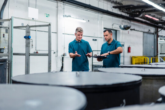 Mature male engineer discussing with colleague about containers while walking in industry