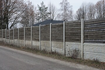 long gray white wall of wooden private fence wall in street by asphalt road