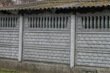 part of a gray concrete wall of a fence outside under a slate roof