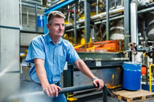 Confident mature businessman looking away while leaning on railing in factory