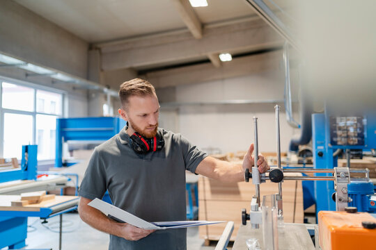 Portrait of carpenter inspecting machines in production hall with ring binder in hand