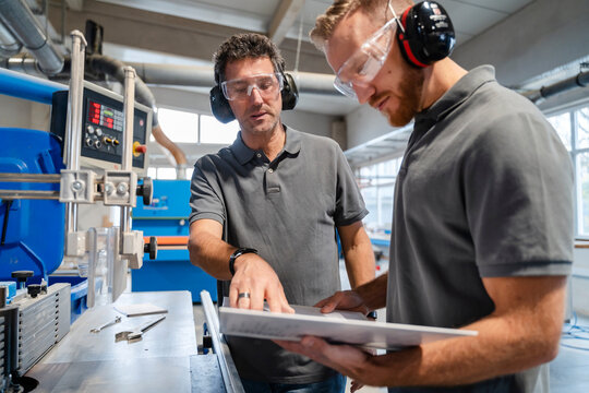 Two male carpenters talking over documents in production hall