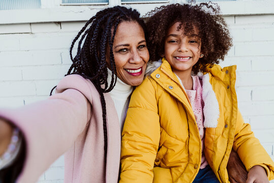 Close-up portrait of mother and daughter sitting against wall