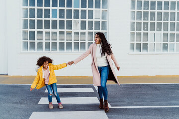 Cheerful mother and daughter holding hands while walking on road against building