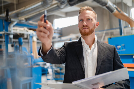 Portrait of&not;&dagger;well-dressed&not;&dagger;carpenter standing in production hall with ring binder in hands