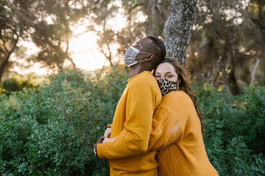 Woman wearing protective face mask hugging man while standing at forest