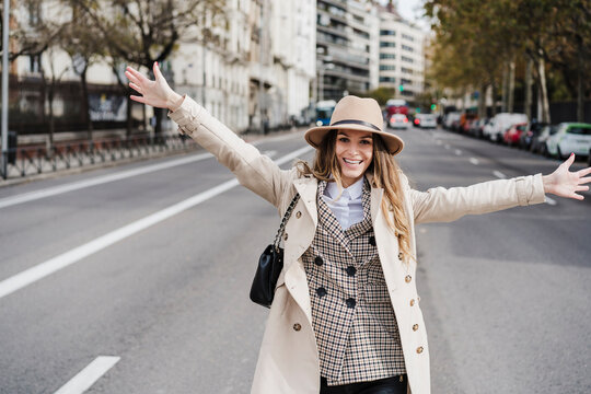 Happy Fashionable Woman With Arms Raised Standing On Road In City