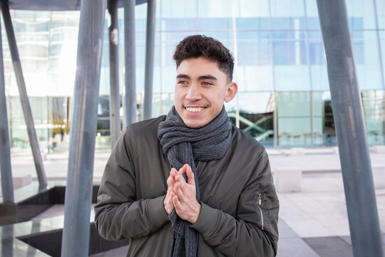 Smiling young man with hands clasped looking away while standing against building