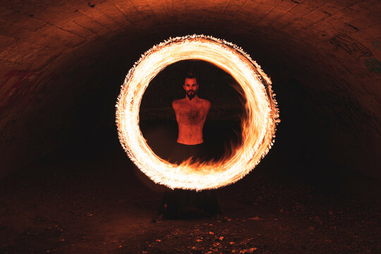 Hipster male performing fire ring in tunnel