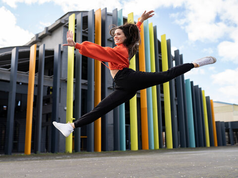 Portrait of beautiful brunette jumping in front of colorful building