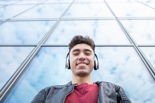 Happy young man listening music against glass building