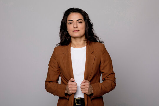 Woman with brown blazer jacket standing against gray background