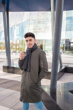 Smiling young man with hands in pockets holding coffee cup against building in city