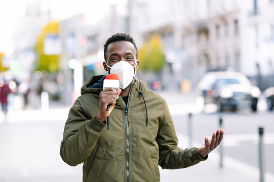 Male presenter wearing face mask talking over microphone while standing in city