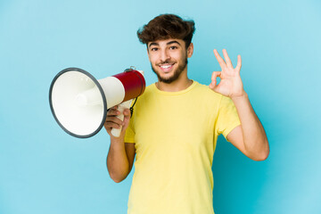 Young arab man holding a megaphone cheerful and confident showing ok gesture.