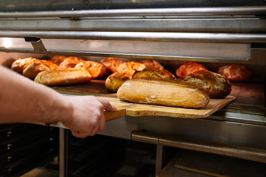 Male chef removing baked breads with pizza peel from oven in bakery