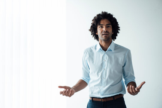 Confident young handsome male entrepreneur giving presentation against white wall at office