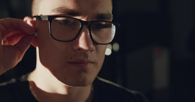 Close view of man in glasses wears wireless headphones on ears indoors