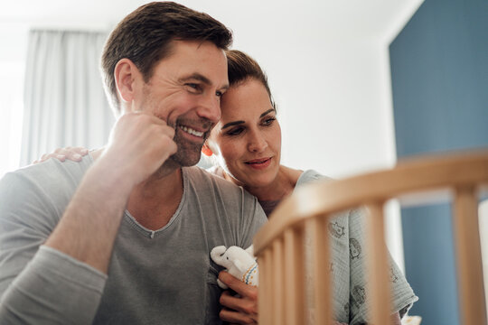 Happy mature couple with stuffed elephant toy looking at crib in bedroom