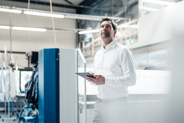 Male inspector with digital tablet examining equipment while standing at industry